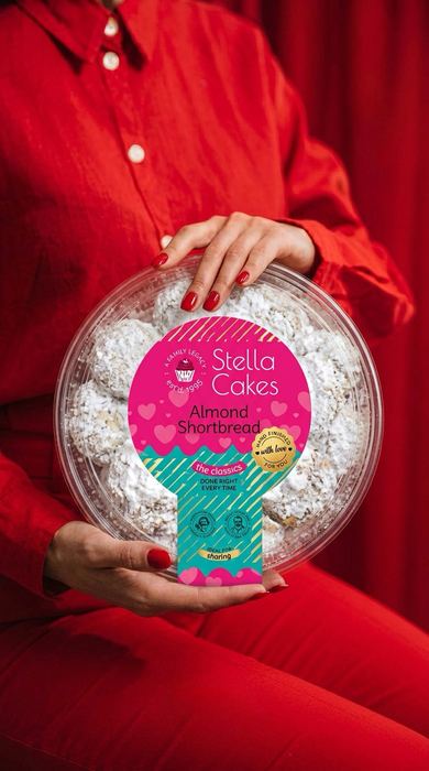A woman in a red outfit holding a tub of Stella Cakes Almond Shortbread